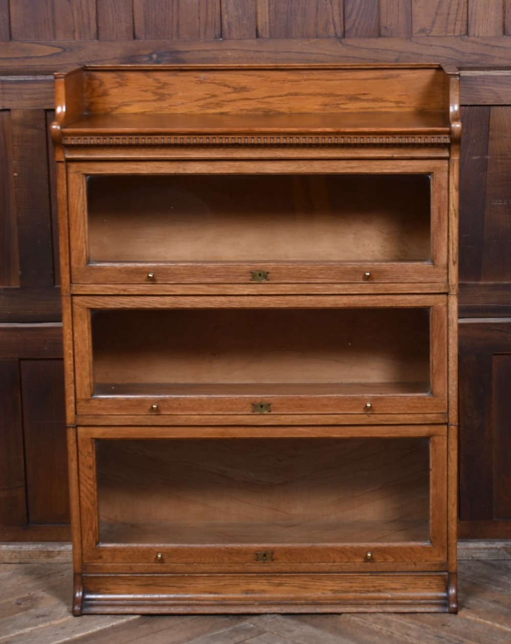 A three-tier Edwardian oak sectional bookcase featuring glass up-and-over doors with small brass knobs and a galleried top.