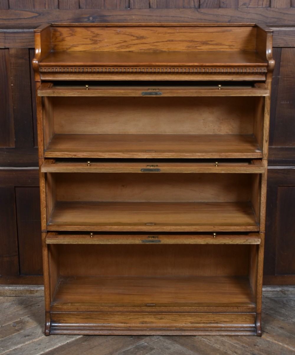 A three-tier Edwardian oak sectional bookcase featuring glass up-and-over doors with small brass knobs and a galleried top. View IX