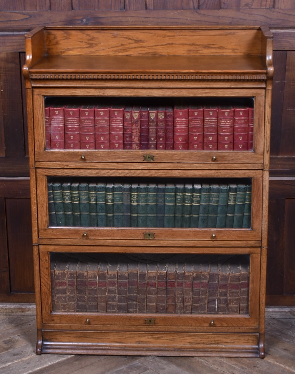 A three-tier Edwardian oak sectional bookcase featuring glass up-and-over doors with small brass knobs and a galleried top. View XII