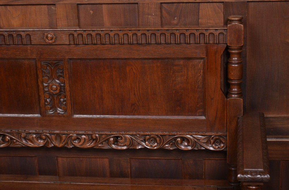 A dark carved oak hall bench featuring a panelled backrest, turned arm supports, and a hinged box storage seat. View II