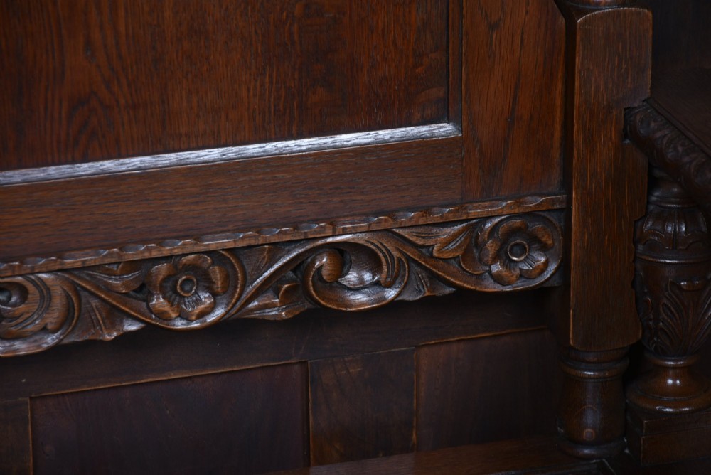 A dark carved oak hall bench featuring a panelled backrest, turned arm supports, and a hinged box storage seat. View VIII
