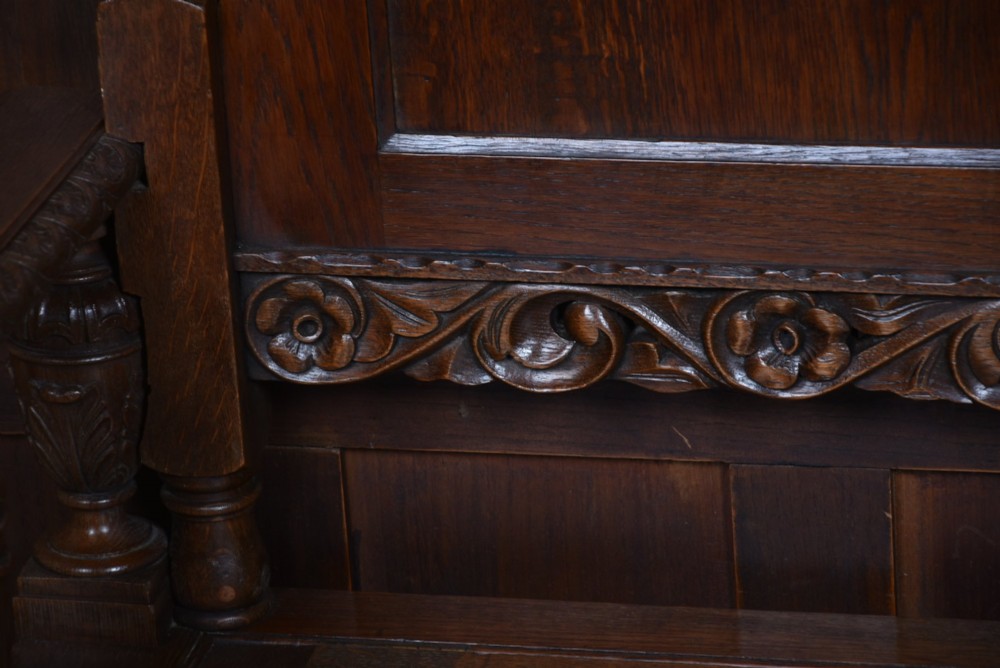 A dark carved oak hall bench featuring a panelled backrest, turned arm supports, and a hinged box storage seat. View IX