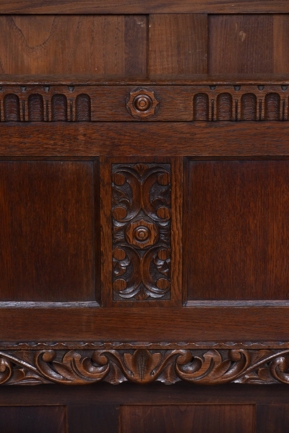 A dark carved oak hall bench featuring a panelled backrest, turned arm supports, and a hinged box storage seat. View X