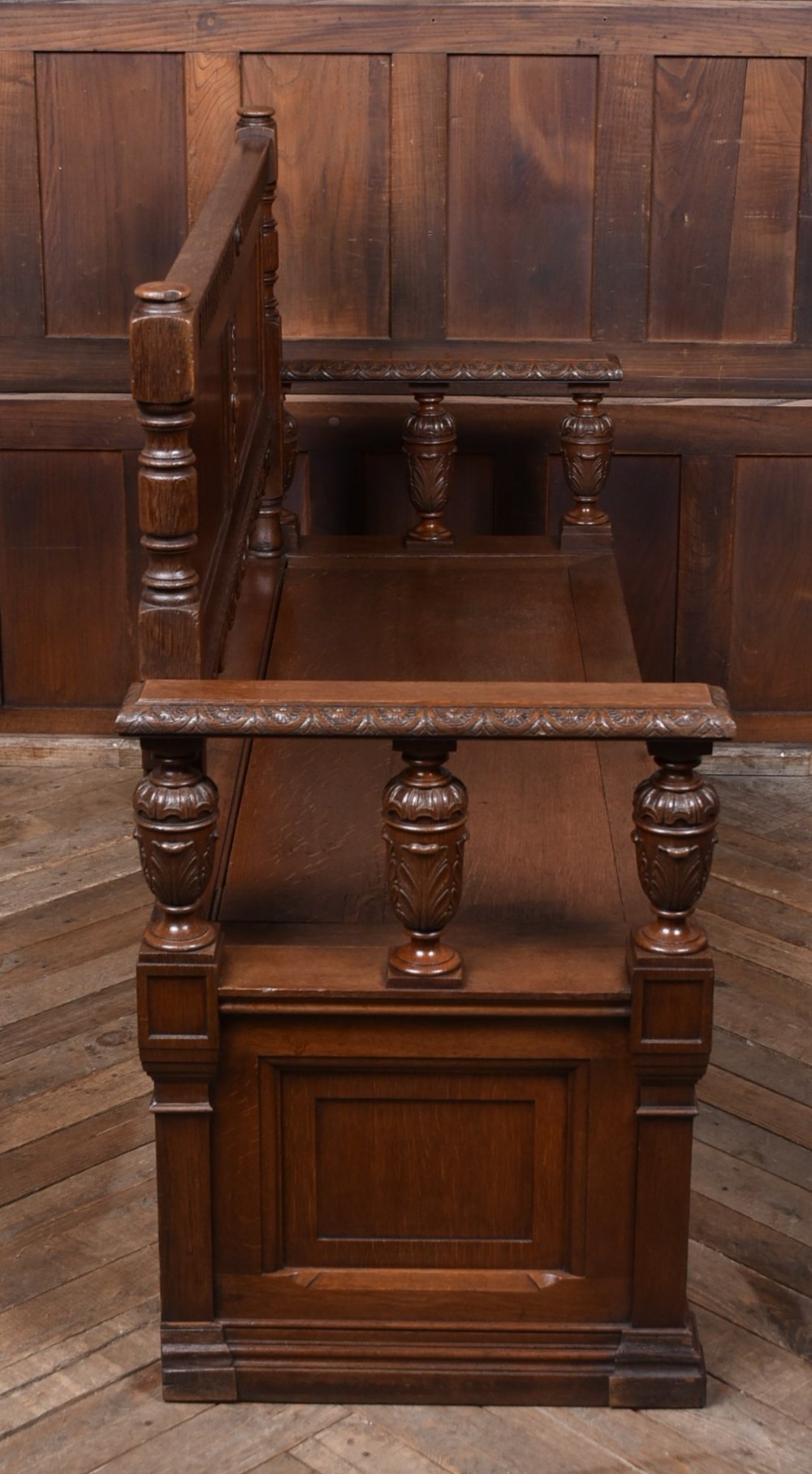 A dark carved oak hall bench featuring a panelled backrest, turned arm supports, and a hinged box storage seat. View XI