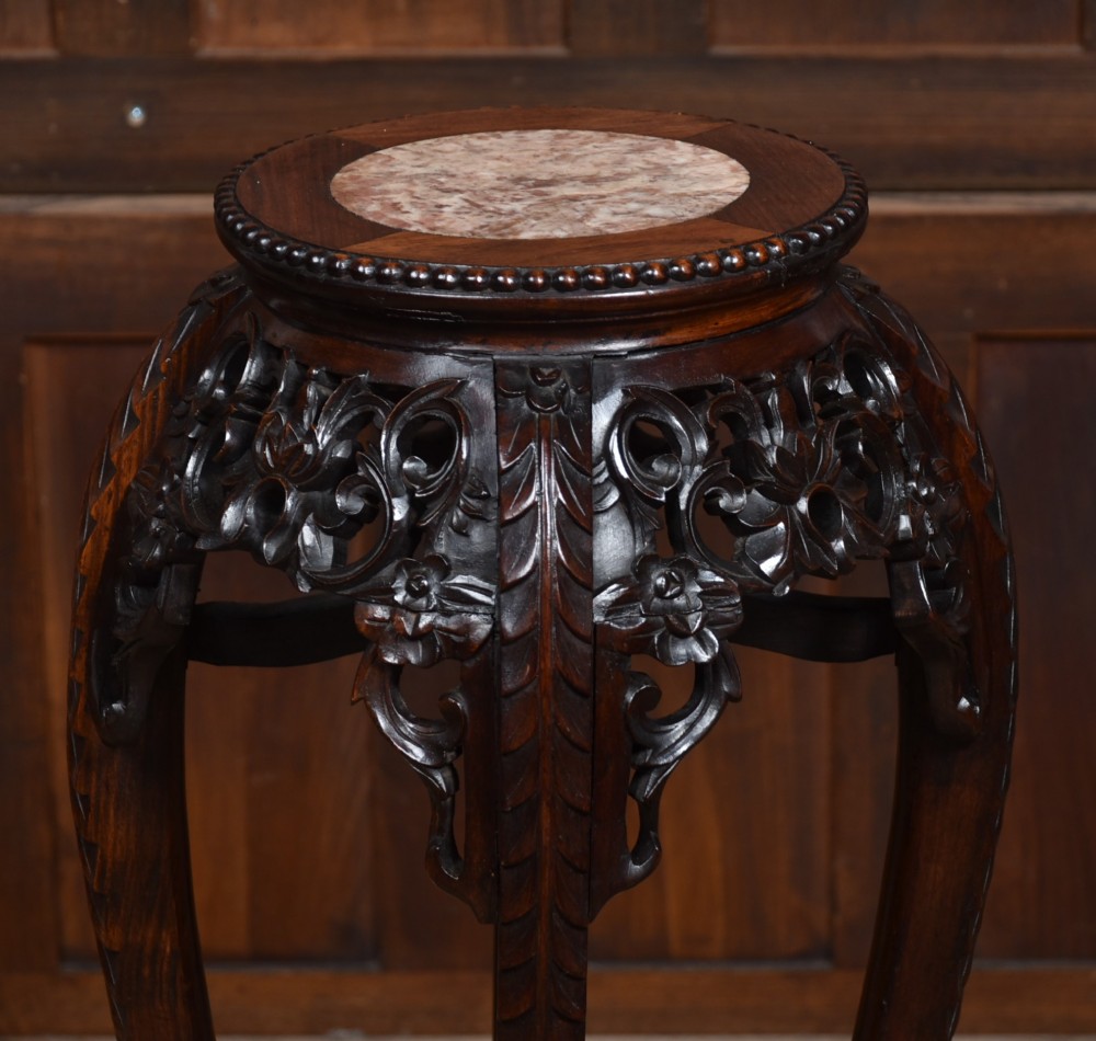 A tall dark hardwood Chinese plant stand featuring a round inset marble top, intricately carved floral aprons, and long swept legs joined by a lower central stretcher. View II