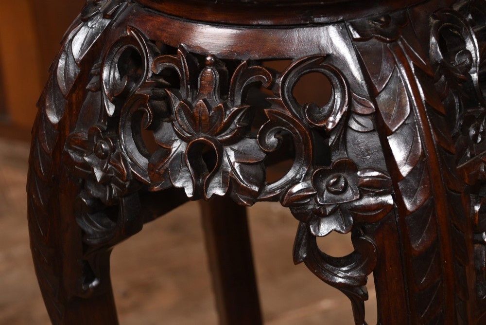 A tall dark hardwood Chinese plant stand featuring a round inset marble top, intricately carved floral aprons, and long swept legs joined by a lower central stretcher. View VIII