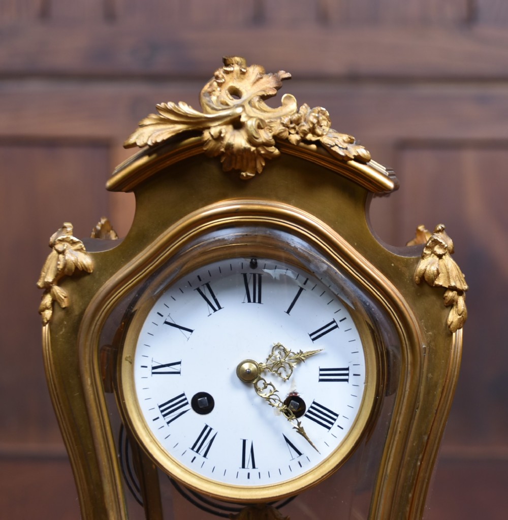 A 19th-century French gilt bronze mantel clock featuring curved glass panels, a white enamel dial with Roman numerals, and an oval portrait miniature pendulum signed Rodier. View III
