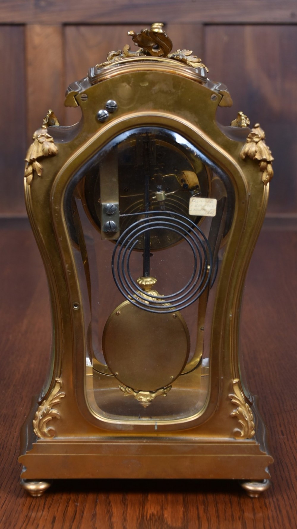 A 19th-century French gilt bronze mantel clock featuring curved glass panels, a white enamel dial with Roman numerals, and an oval portrait miniature pendulum signed Rodier. View VII