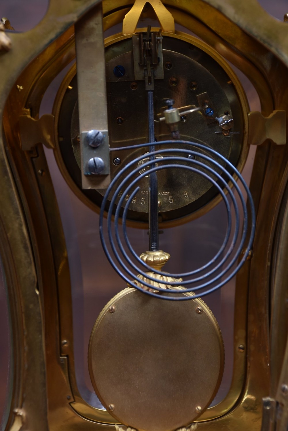 A 19th-century French gilt bronze mantel clock featuring curved glass panels, a white enamel dial with Roman numerals, and an oval portrait miniature pendulum signed Rodier. View IX
