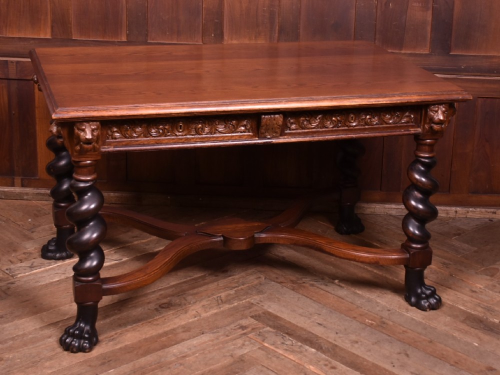 A 19th-century dark oak library table featuring barley twist legs, carved lion mask corners, an intricate apron, and an X-frame stretcher resting on paw feet.
