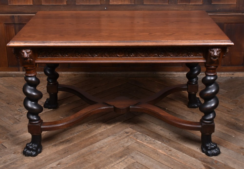 A 19th-century dark oak library table featuring barley twist legs, carved lion mask corners, an intricate apron, and an X-frame stretcher resting on paw feet. View X