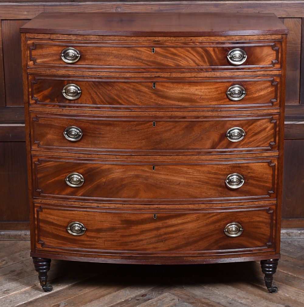 An early nineteenth-century mahogany bow-front chest of drawers featuring five graduated drawers with oval brass handles and turned feet.