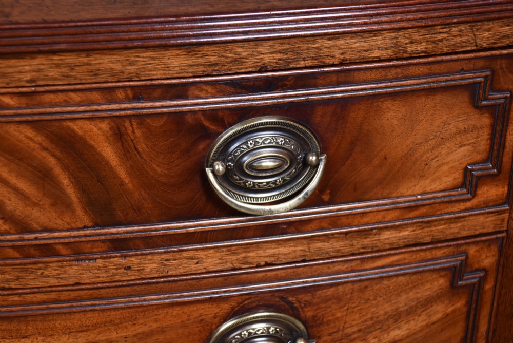 An early nineteenth-century mahogany bow-front chest of drawers featuring five graduated drawers with oval brass handles and turned feet. View II