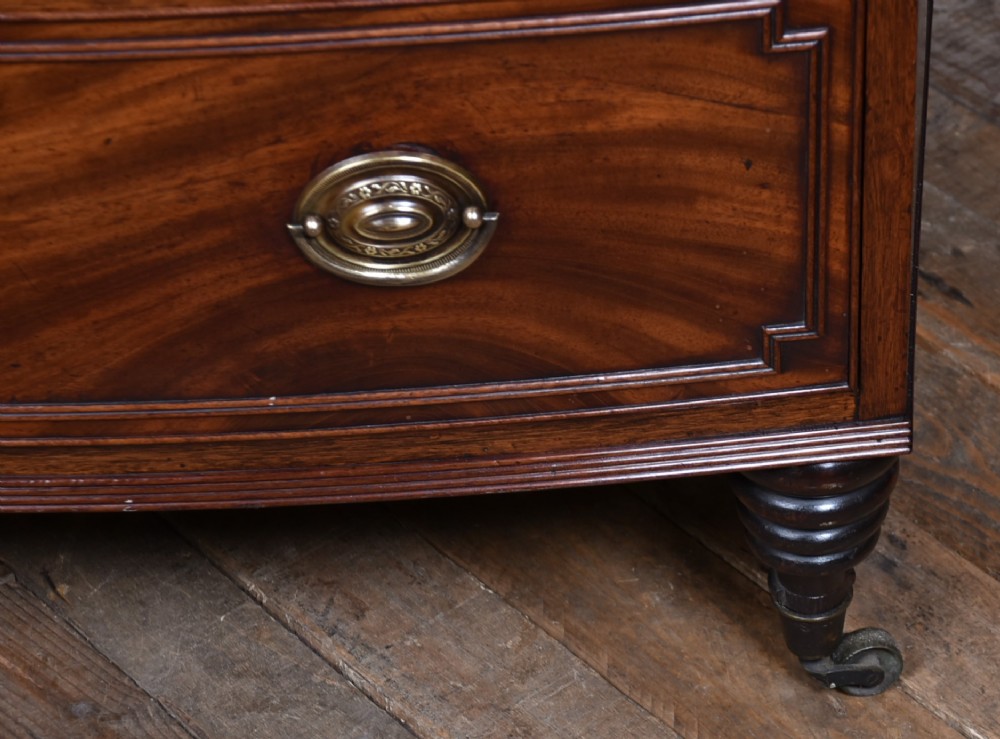 An early nineteenth-century mahogany bow-front chest of drawers featuring five graduated drawers with oval brass handles and turned feet. View IV