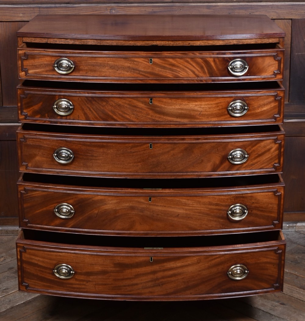An early nineteenth-century mahogany bow-front chest of drawers featuring five graduated drawers with oval brass handles and turned feet. View V