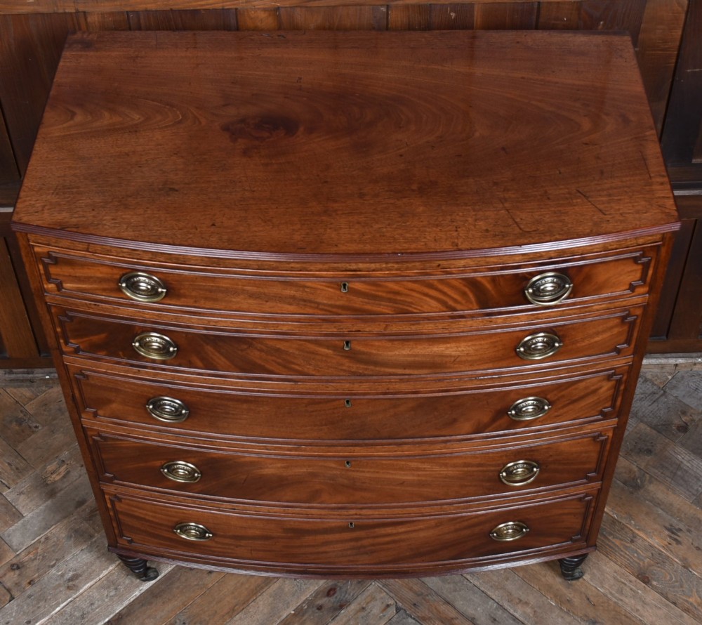 An early nineteenth-century mahogany bow-front chest of drawers featuring five graduated drawers with oval brass handles and turned feet. View VI