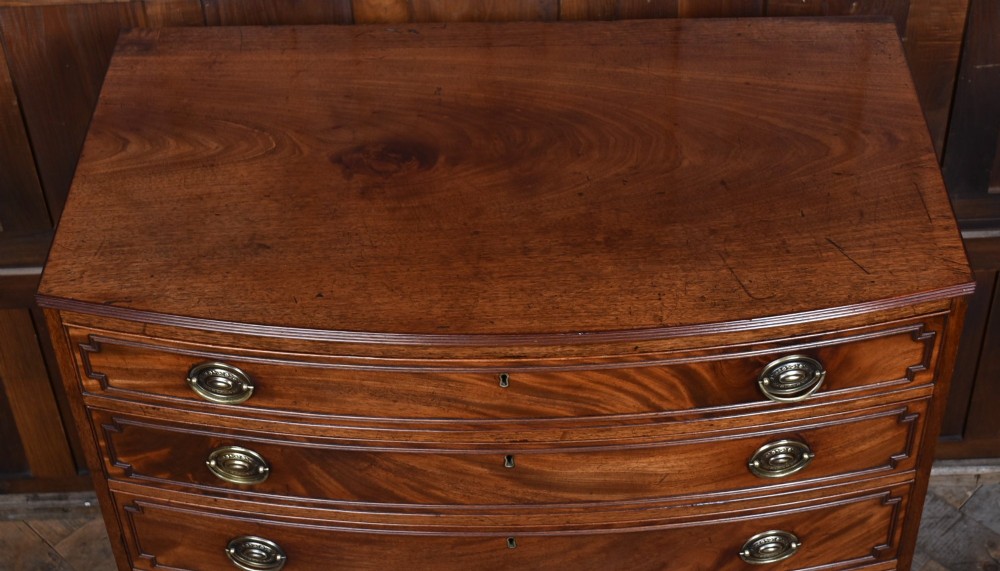 An early nineteenth-century mahogany bow-front chest of drawers featuring five graduated drawers with oval brass handles and turned feet. View VII