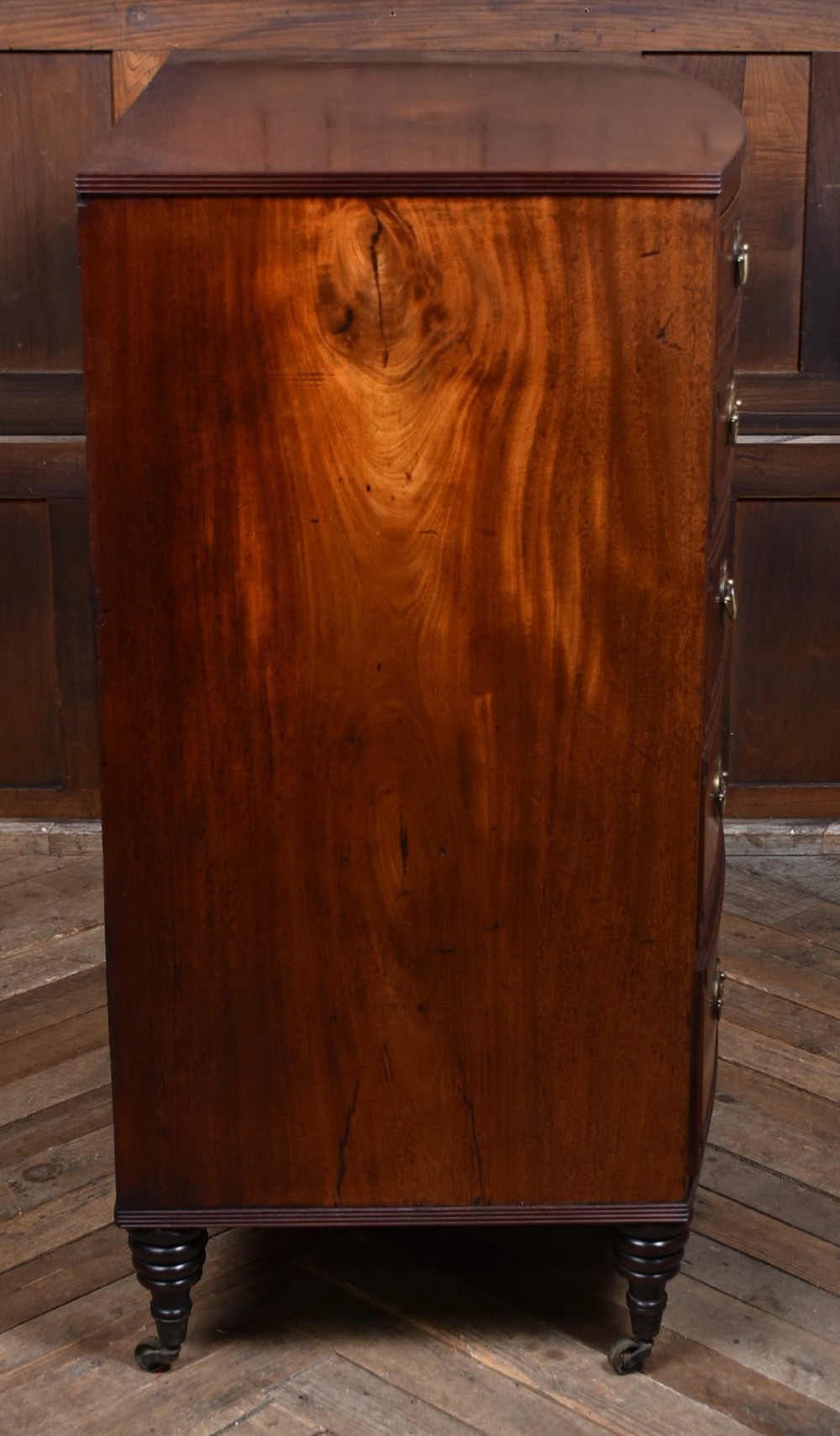 An early nineteenth-century mahogany bow-front chest of drawers featuring five graduated drawers with oval brass handles and turned feet. View VIII
