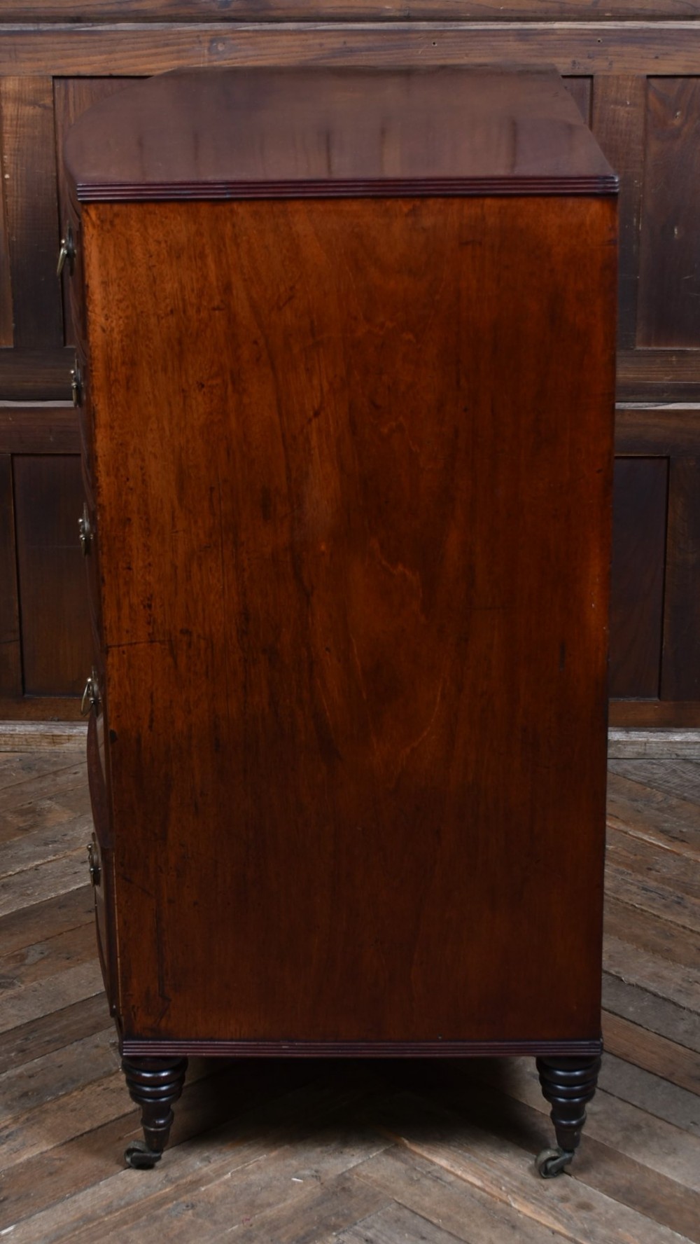 An early nineteenth-century mahogany bow-front chest of drawers featuring five graduated drawers with oval brass handles and turned feet. View X