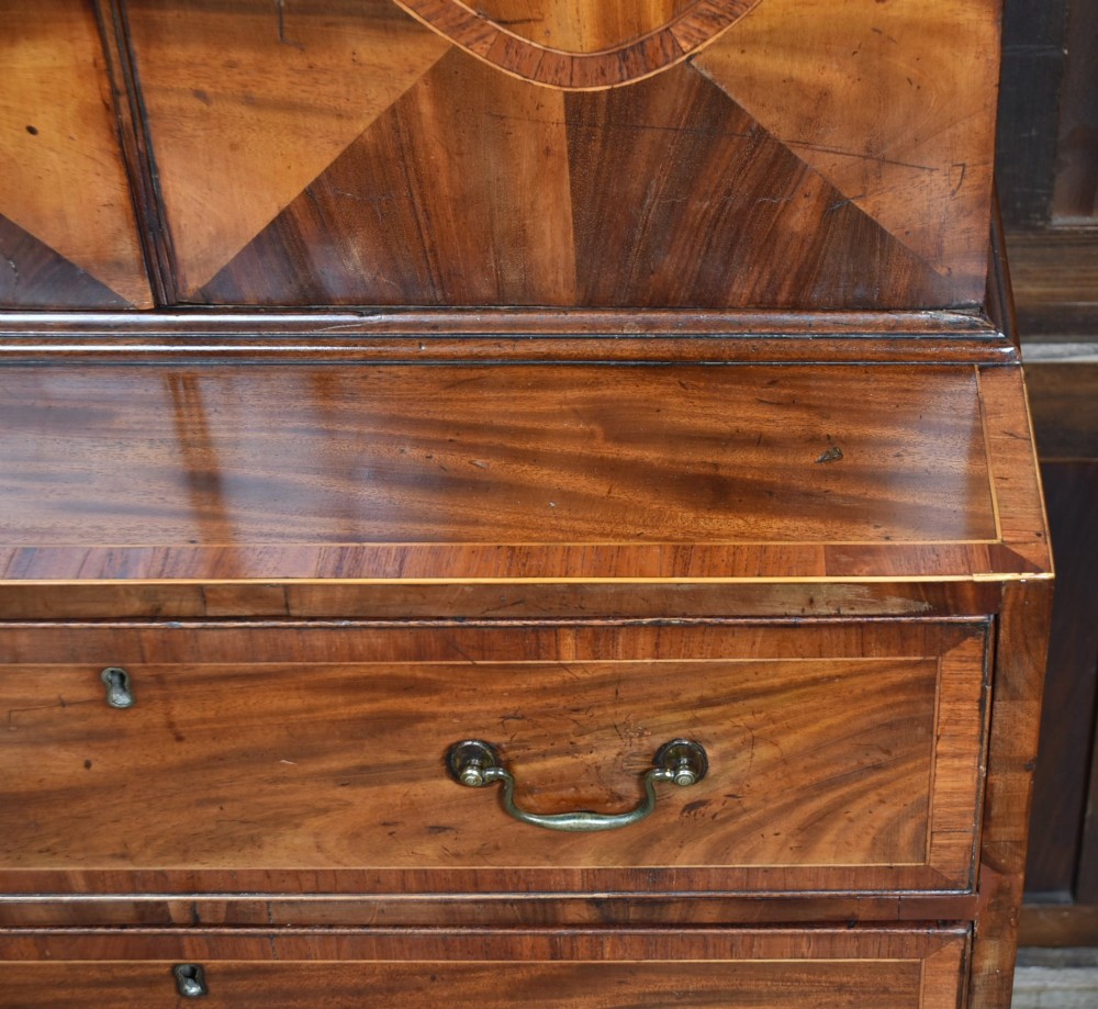 A tall Georgian mahogany secretaire bookcase featuring an upper two-door cabinet with oval inlay panels above a lower chest with four drawers and brass swan-neck handles. View XIV