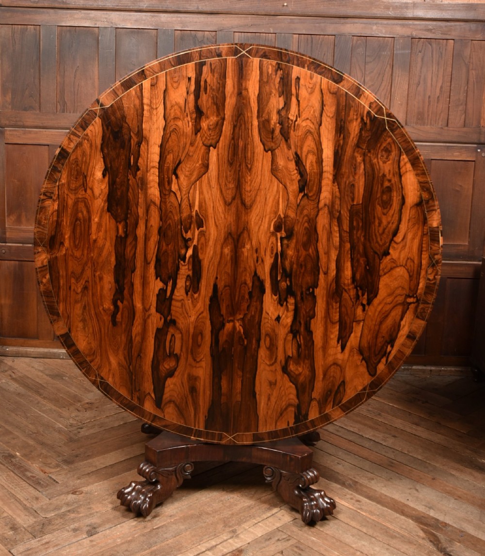 A circular Victorian rosewood tilt-top table featuring highly figured timber grain, a deep apron, a carved central pedestal column, and a quadform base on carved claw feet. View II