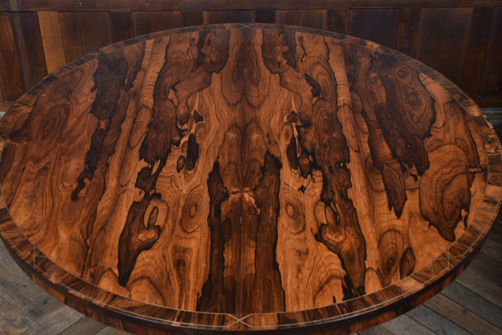 A circular Victorian rosewood tilt-top table featuring highly figured timber grain, a deep apron, a carved central pedestal column, and a quadform base on carved claw feet. View VII