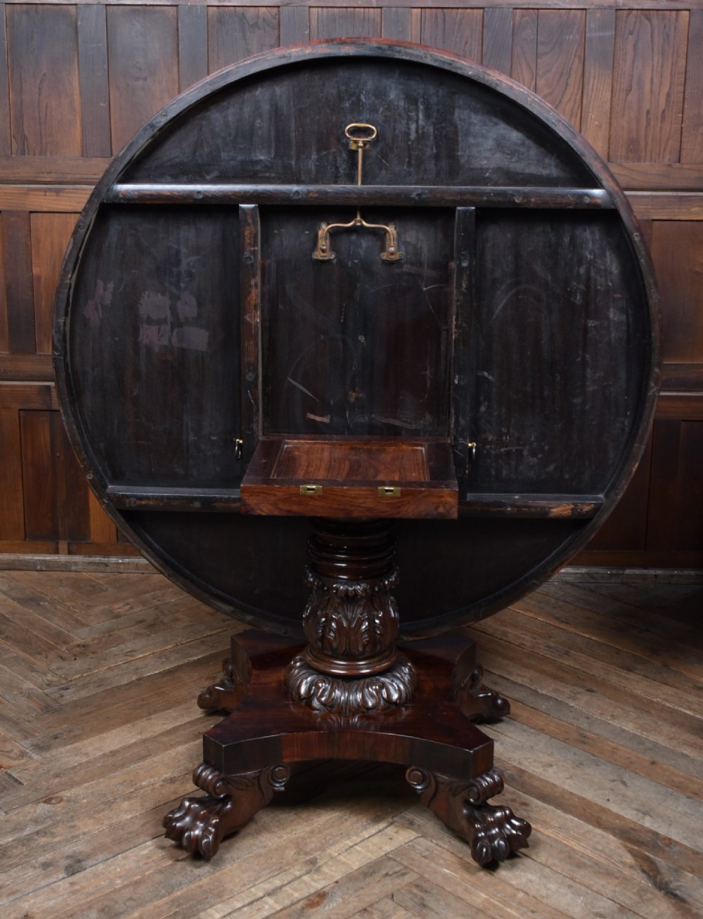 A circular Victorian rosewood tilt-top table featuring highly figured timber grain, a deep apron, a carved central pedestal column, and a quadform base on carved claw feet. View IX