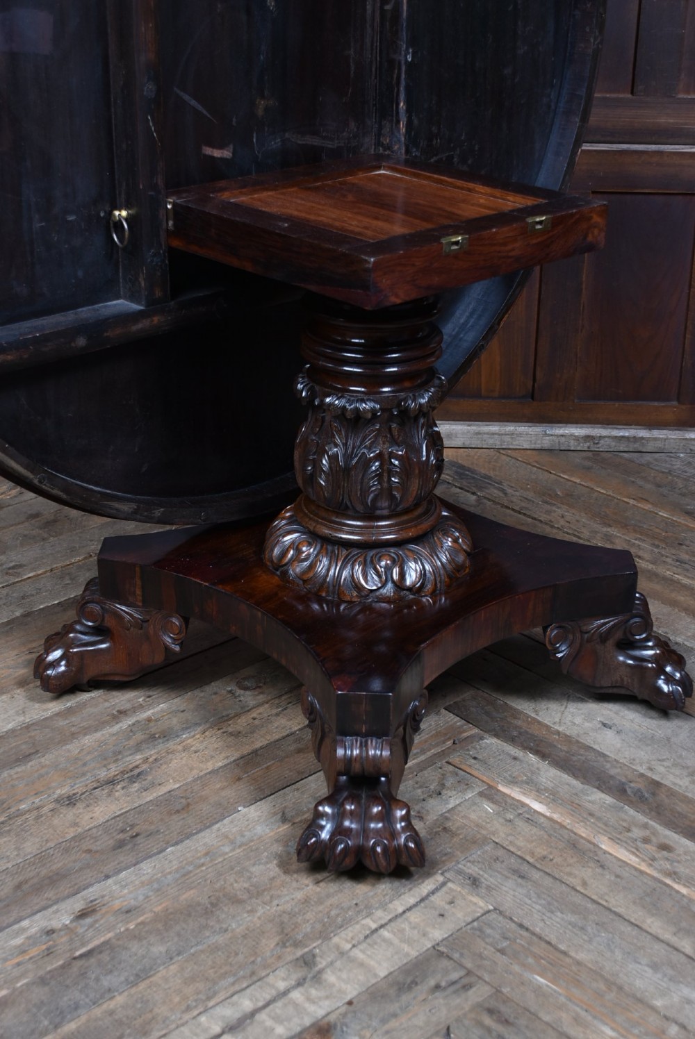 A circular Victorian rosewood tilt-top table featuring highly figured timber grain, a deep apron, a carved central pedestal column, and a quadform base on carved claw feet. View XII