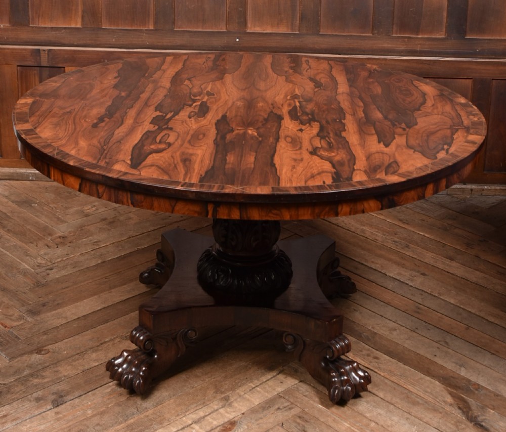 A circular Victorian rosewood tilt-top table featuring highly figured timber grain, a deep apron, a carved central pedestal column, and a quadform base on carved claw feet. View XIII