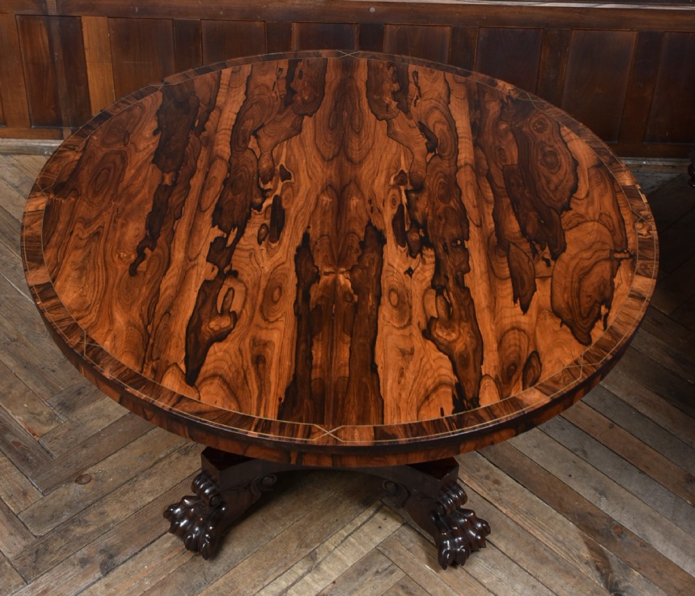 A circular Victorian rosewood tilt-top table featuring highly figured timber grain, a deep apron, a carved central pedestal column, and a quadform base on carved claw feet. View XIV