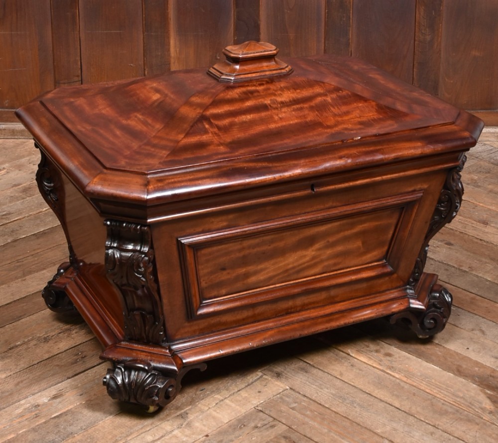 A Victorian mahogany sarcophagus-shaped cellarette featuring carved corner pilasters, a stepped hinged lid, and carved scroll feet.