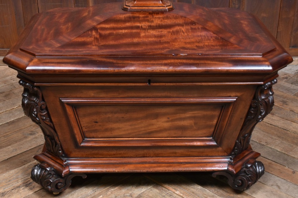A Victorian mahogany sarcophagus-shaped cellarette featuring carved corner pilasters, a stepped hinged lid, and carved scroll feet. View III