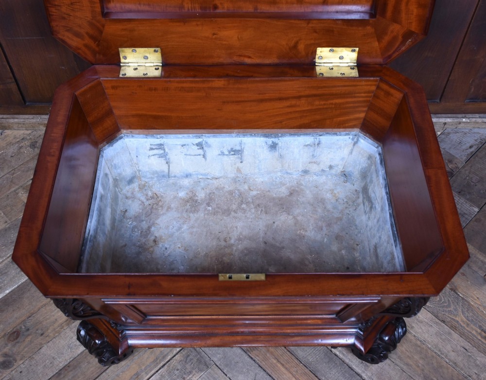 A Victorian mahogany sarcophagus-shaped cellarette featuring carved corner pilasters, a stepped hinged lid, and carved scroll feet. View VII