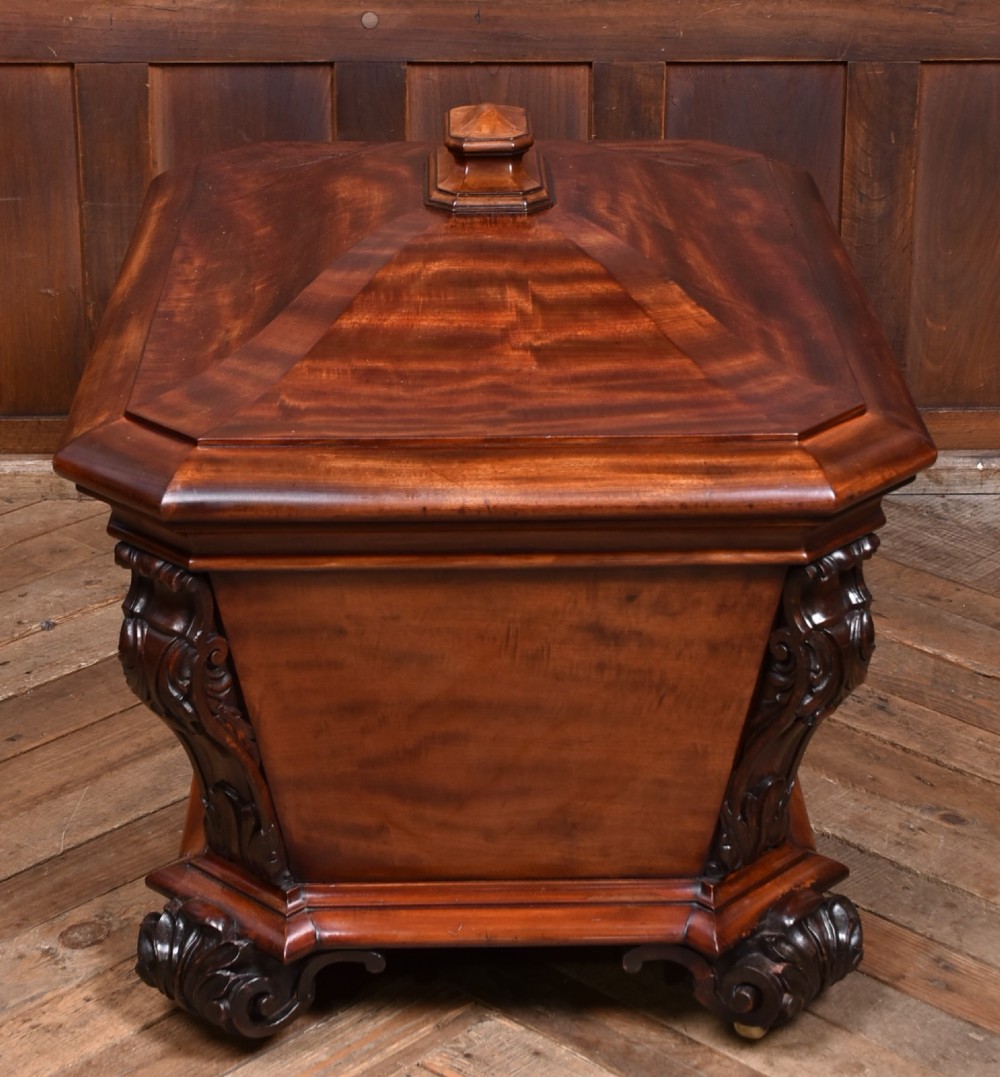 A Victorian mahogany sarcophagus-shaped cellarette featuring carved corner pilasters, a stepped hinged lid, and carved scroll feet. View VIII