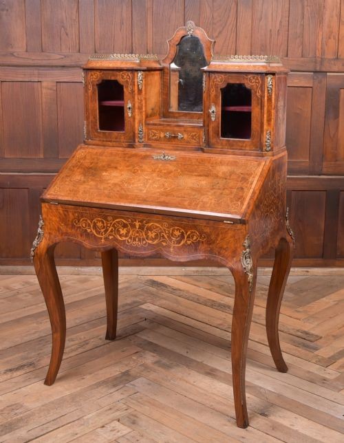An antique French walnut ladys writing desk featuring floral marquetry, cabriole legs, brass mounts, and a raised upper section with glass cabinets and a central mirror.