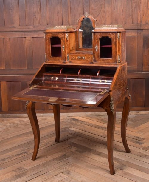 An antique French walnut ladys writing desk featuring floral marquetry, cabriole legs, brass mounts, and a raised upper section with glass cabinets and a central mirror. View V