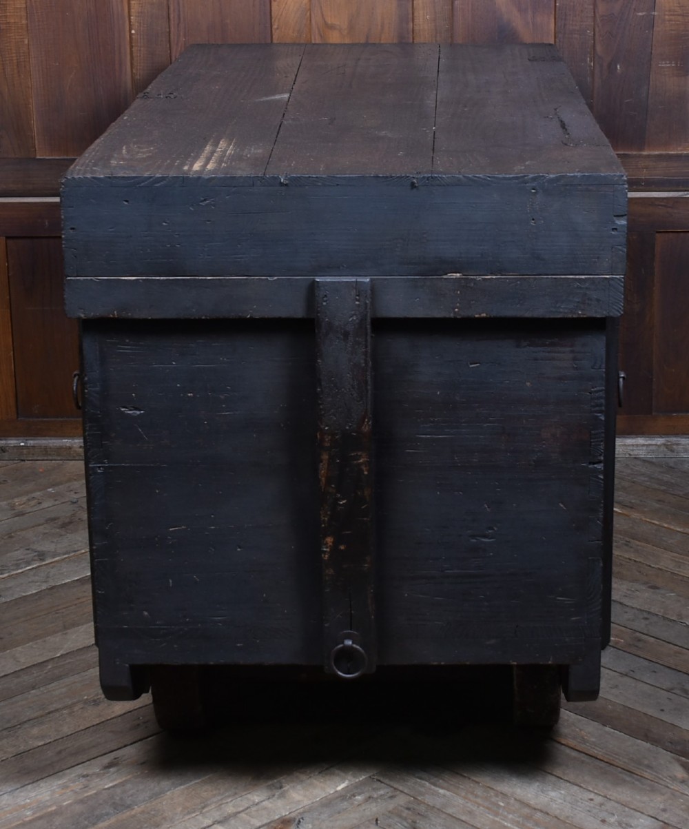 A dark brown Japanese wooden storage chest set on small wheels with vertical timber battens and hand-forged iron fittings. View X