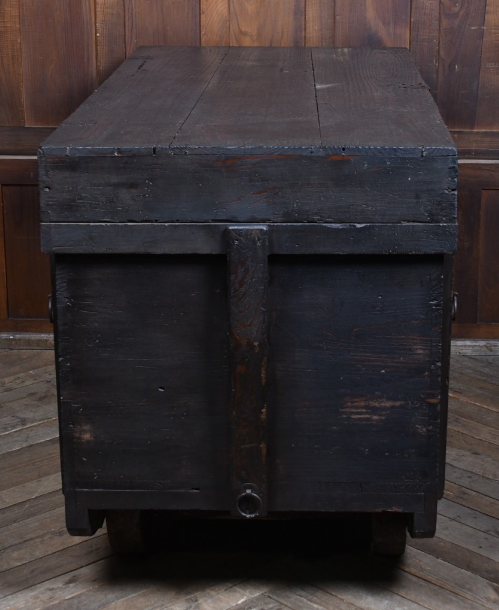 A dark brown Japanese wooden storage chest set on small wheels with vertical timber battens and hand-forged iron fittings. View XII