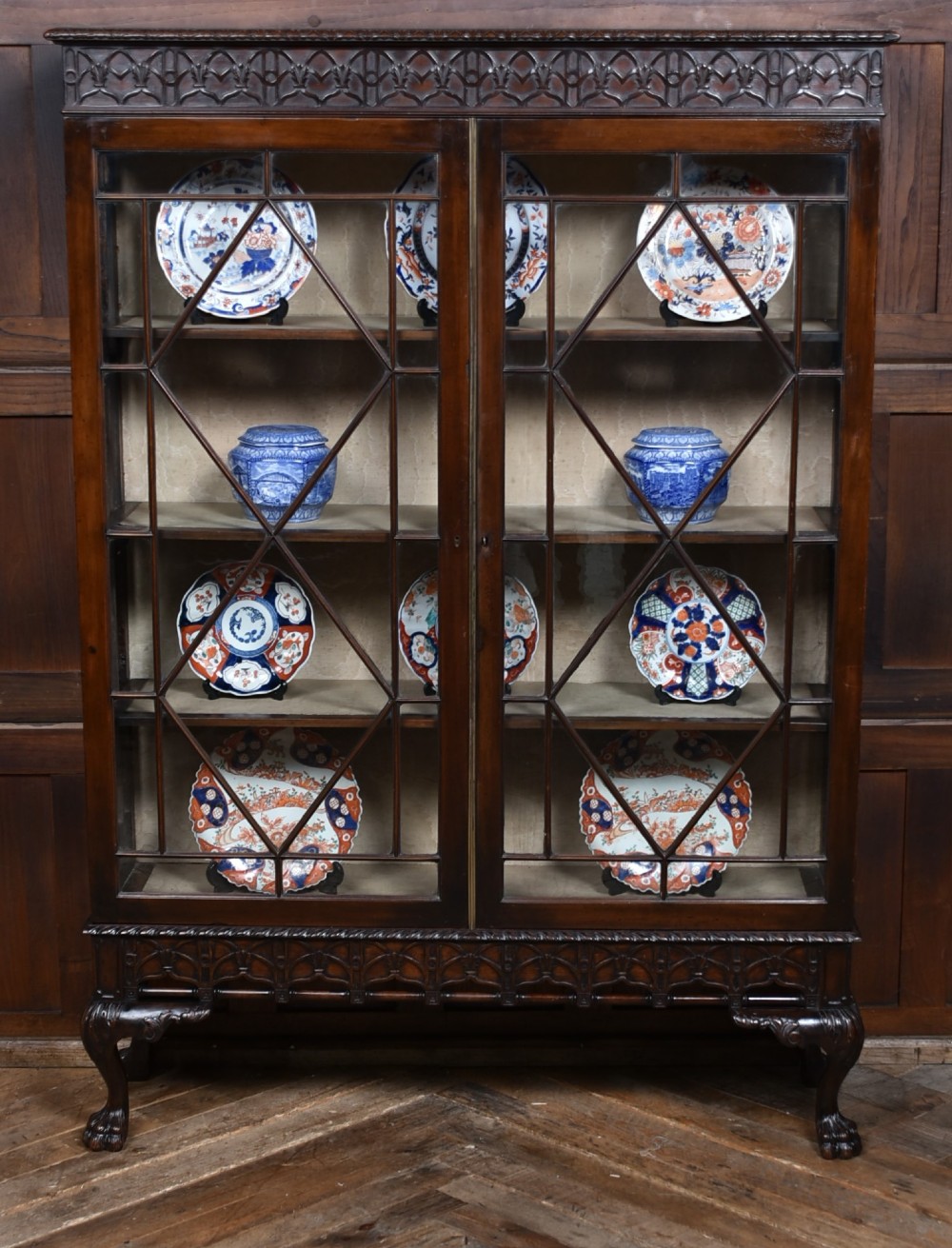 A dark mahogany Chippendale Revival display cabinet featuring double glazed doors with diamond astragal glazing, blind fretwork frieze, and cabriole legs on ball and claw feet.