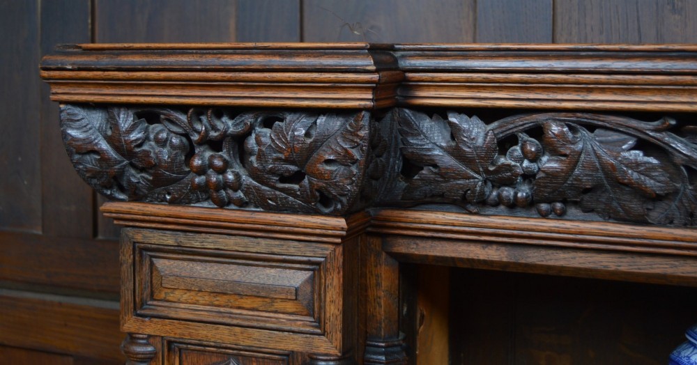 A wide 19th-century Victorian Gothic Revival open oak bookcase featuring detailed floral carvings, moulded pilasters, and twin bays of adjustable wooden shelves. View IV