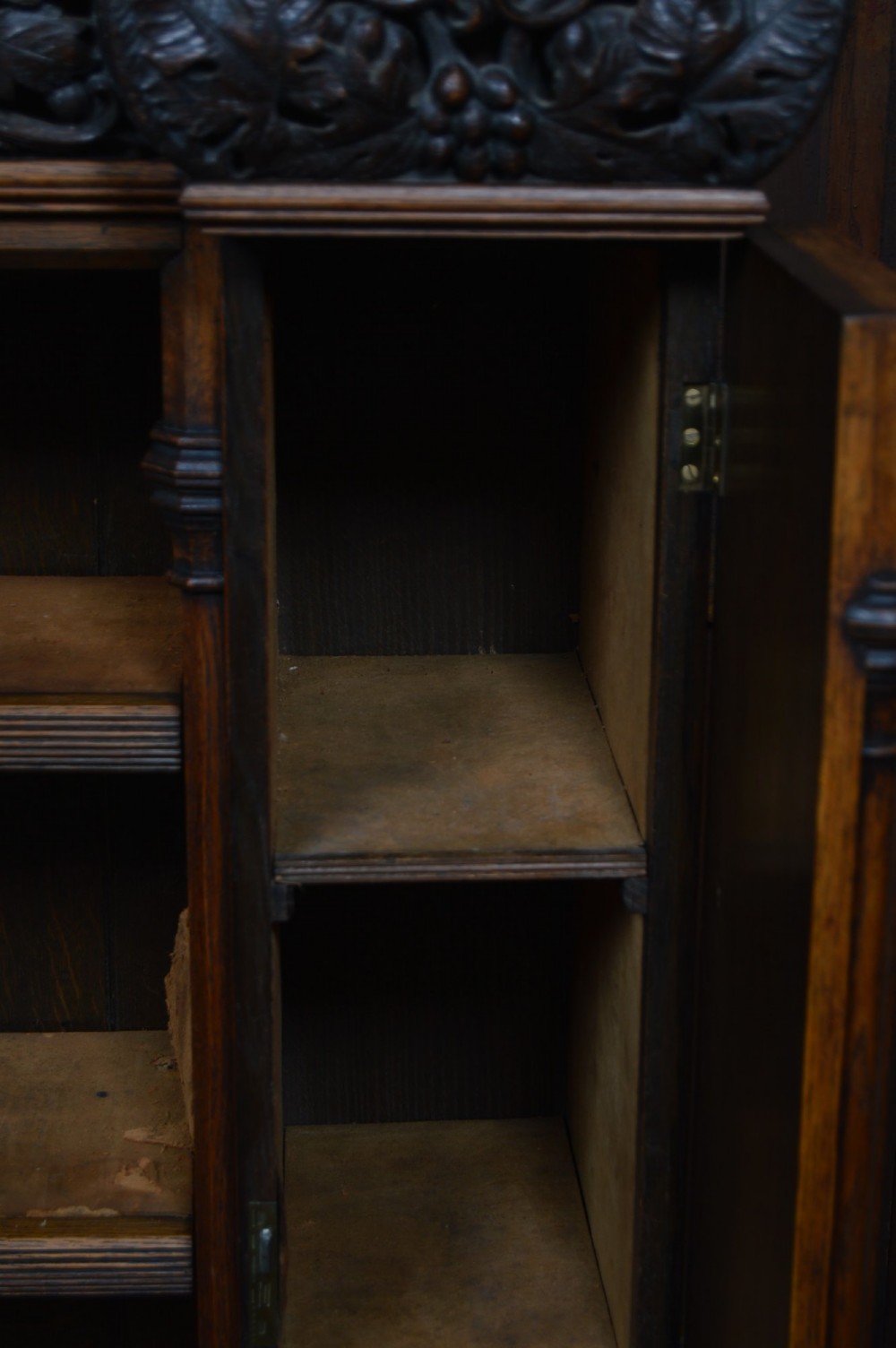 A wide 19th-century Victorian Gothic Revival open oak bookcase featuring detailed floral carvings, moulded pilasters, and twin bays of adjustable wooden shelves. View IX