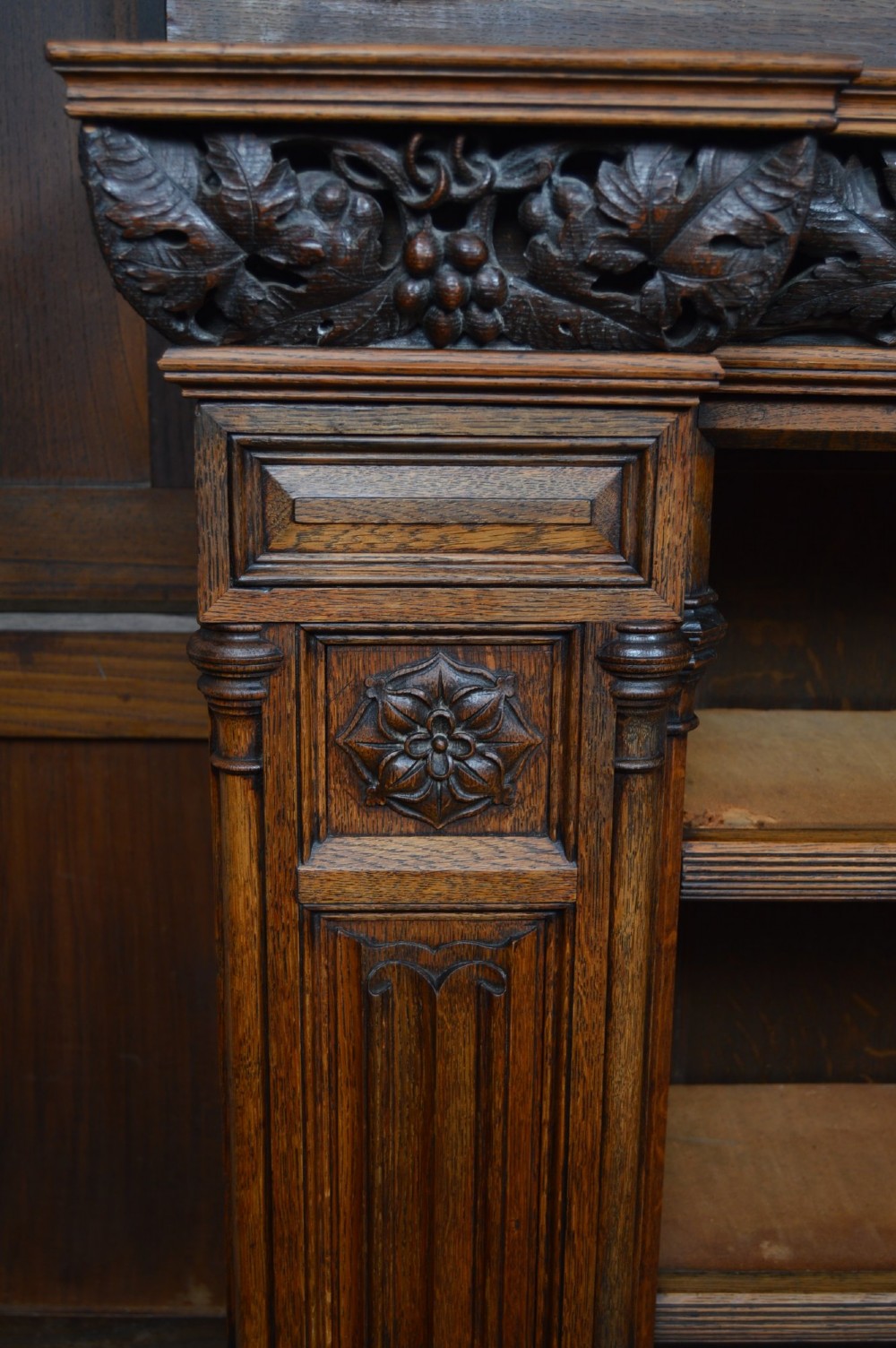 A wide 19th-century Victorian Gothic Revival open oak bookcase featuring detailed floral carvings, moulded pilasters, and twin bays of adjustable wooden shelves. View XII