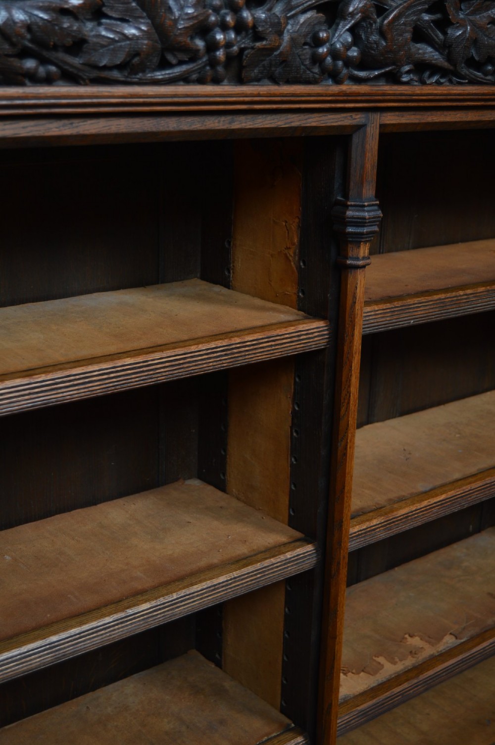 A wide 19th-century Victorian Gothic Revival open oak bookcase featuring detailed floral carvings, moulded pilasters, and twin bays of adjustable wooden shelves. View XIII