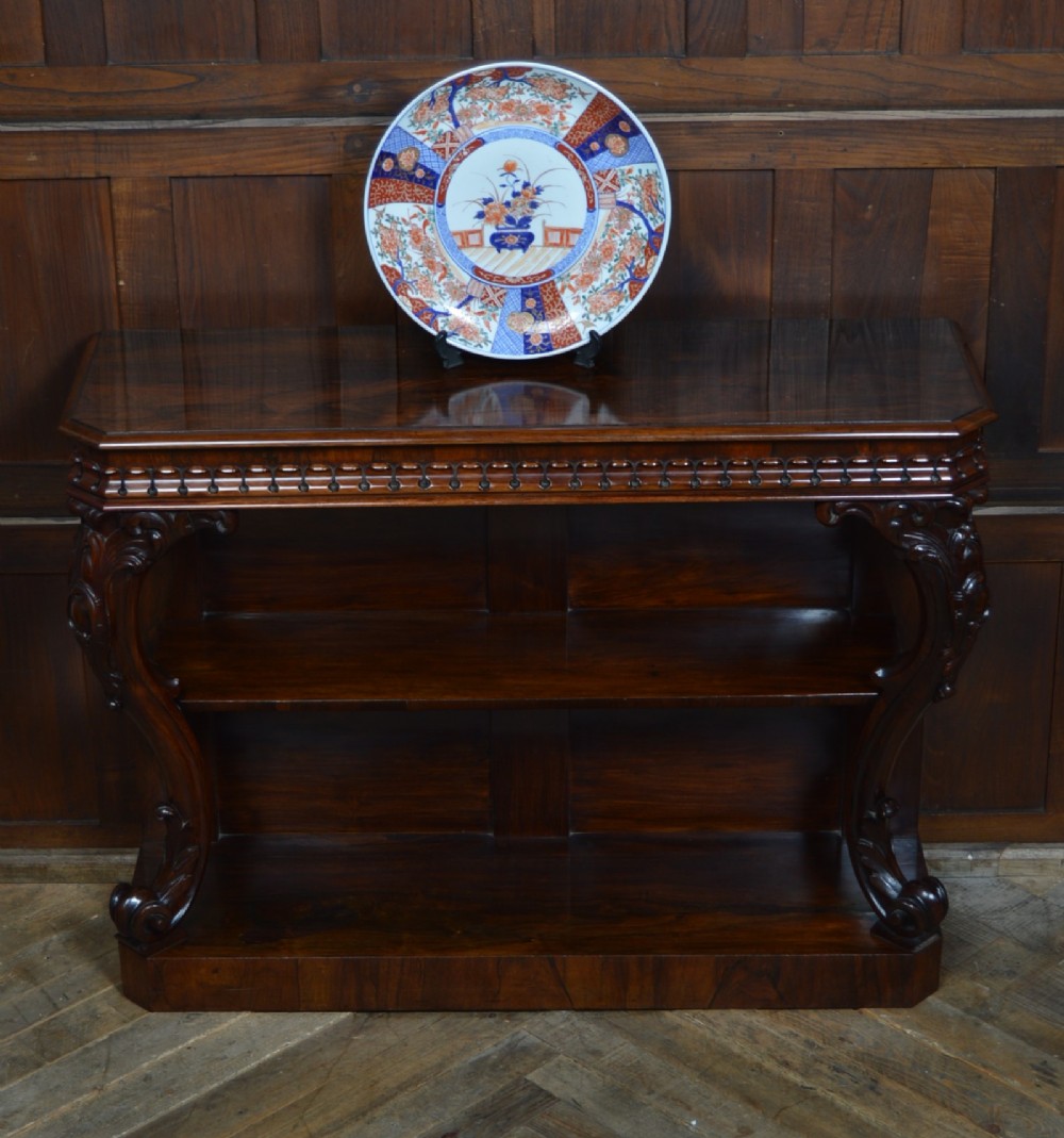 A dark Victorian rosewood console table featuring carved S-scroll supports, an open central shelf, a beaded upper frieze, and a solid plinth base.