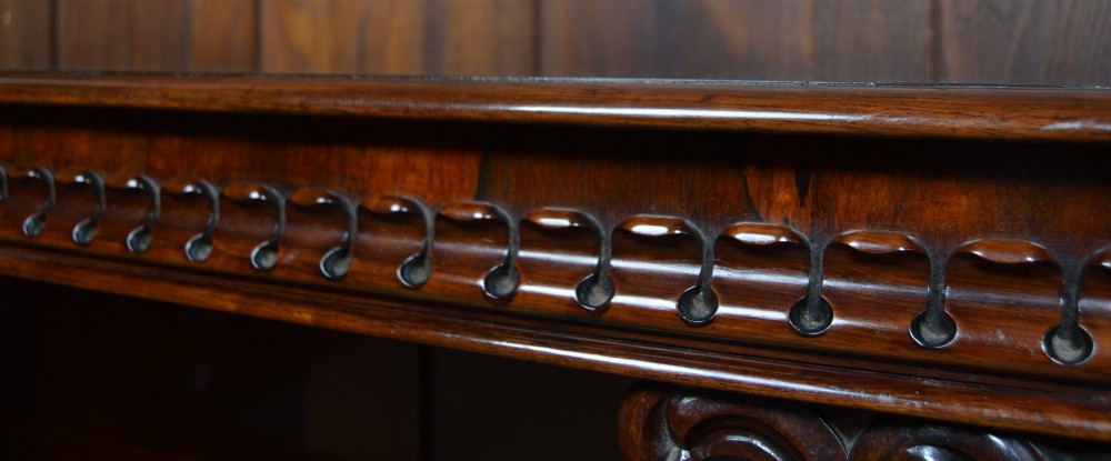 A dark Victorian rosewood console table featuring carved S-scroll supports, an open central shelf, a beaded upper frieze, and a solid plinth base. View IV