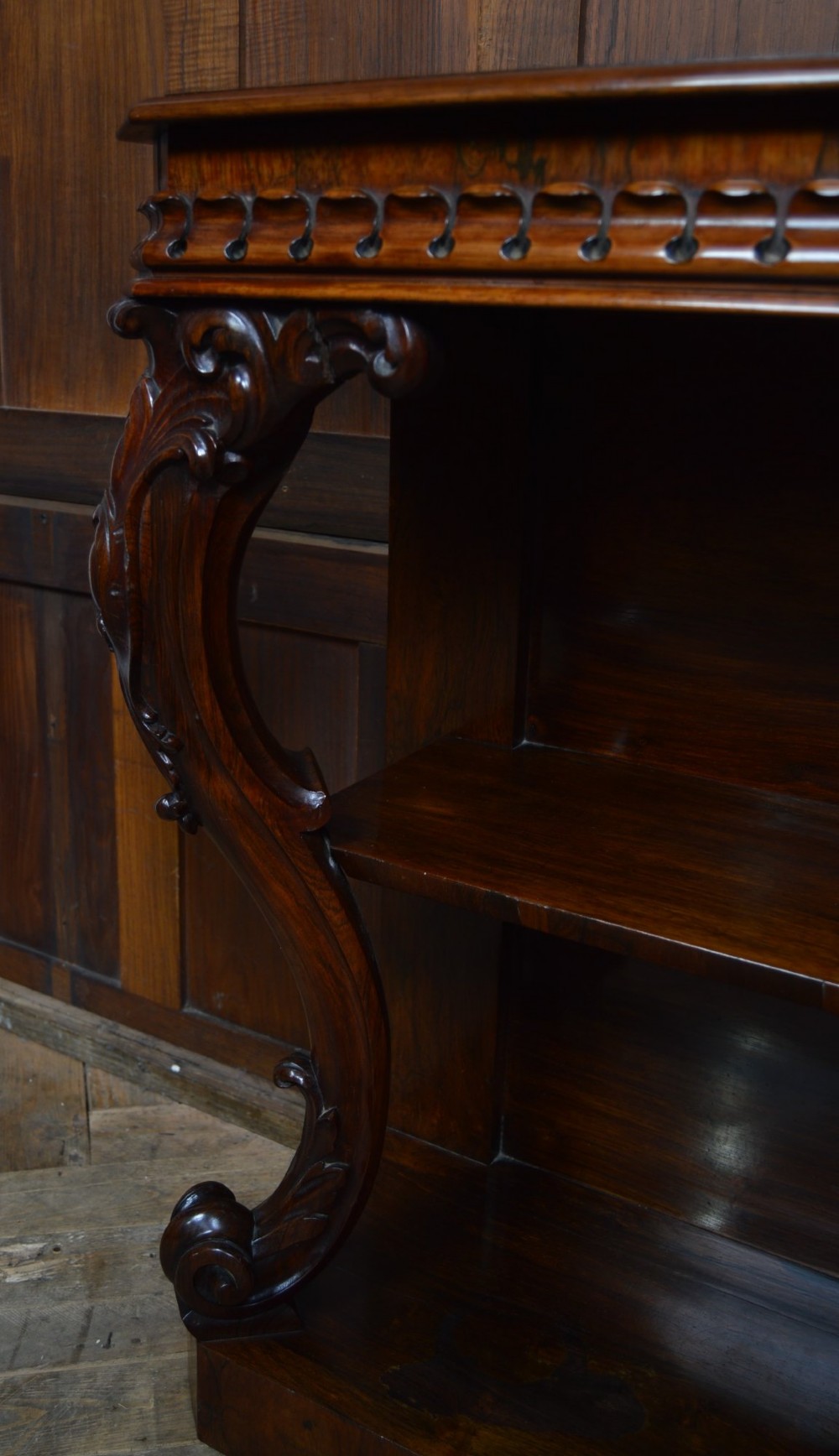 A dark Victorian rosewood console table featuring carved S-scroll supports, an open central shelf, a beaded upper frieze, and a solid plinth base. View V