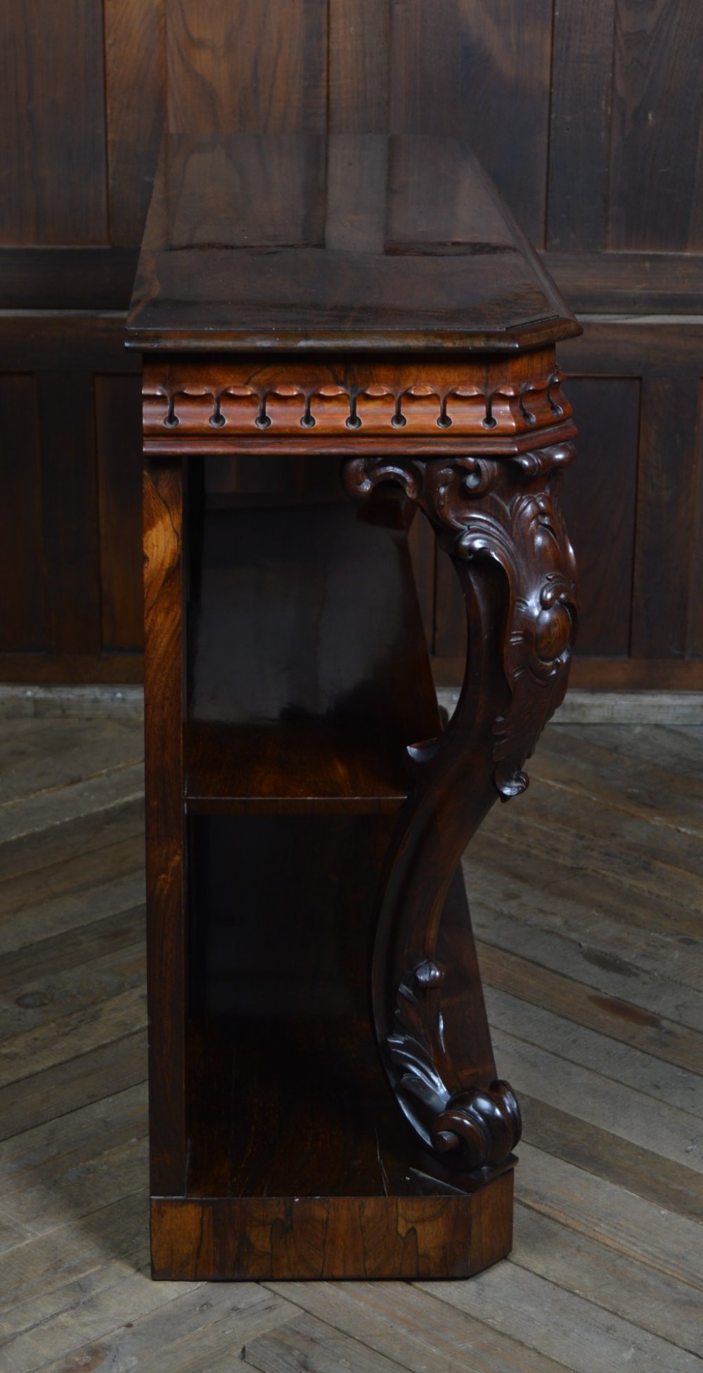 A dark Victorian rosewood console table featuring carved S-scroll supports, an open central shelf, a beaded upper frieze, and a solid plinth base. View VIII