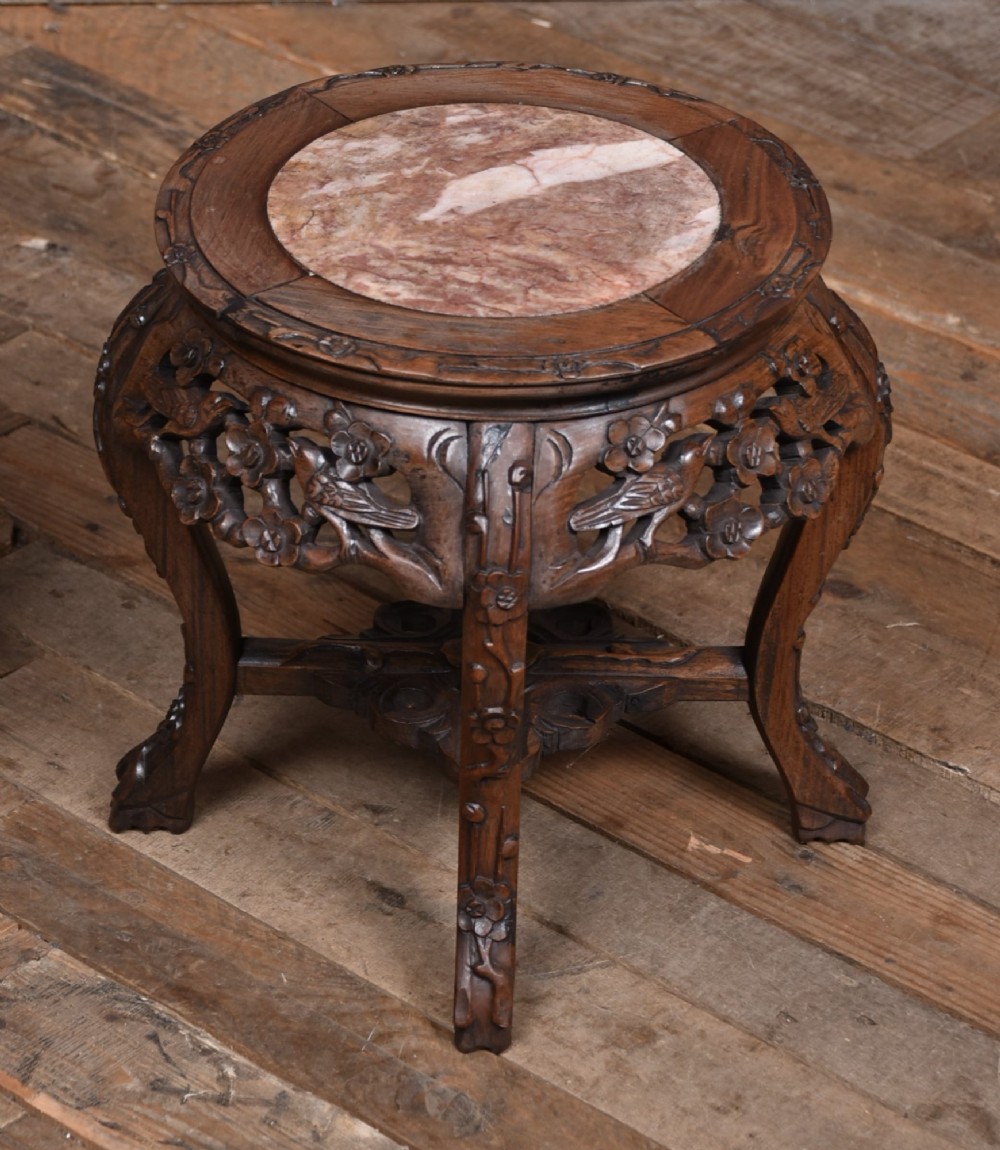A pair of carved dark hardwood round stands featuring inset pink marble tops and pierced floral aprons supported by curved legs. View III