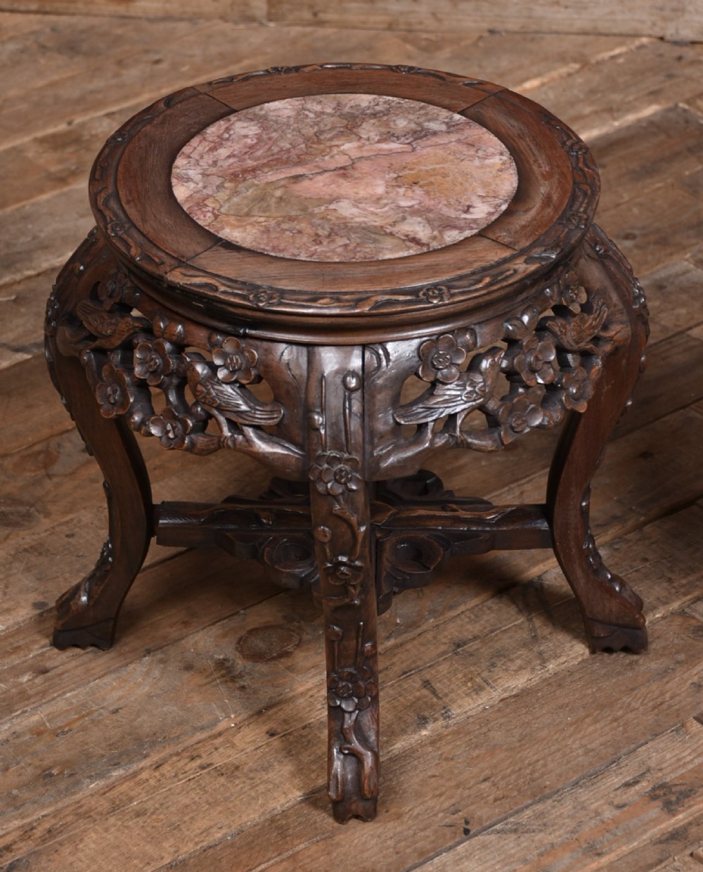 A pair of carved dark hardwood round stands featuring inset pink marble tops and pierced floral aprons supported by curved legs. View IV