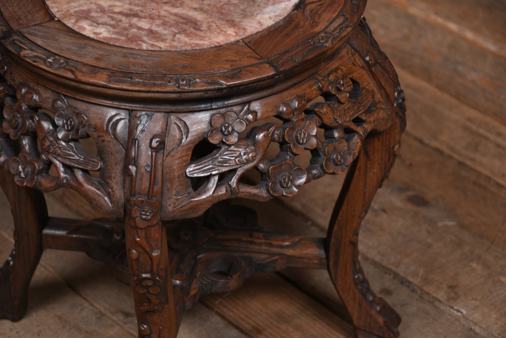 A pair of carved dark hardwood round stands featuring inset pink marble tops and pierced floral aprons supported by curved legs. View V